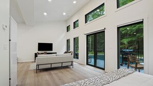 A modern bedroom with a large bed, a TV, and a balcony with outdoor furniture. - New Listing! Luxury Pondside Cabin | Hot Tub (McArthur)