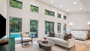 A spacious living room with a large sofa, a coffee table, and a TV. There are multiple windows providing views of the outdoors. - New Listing! Luxury Pondside Cabin | Hot Tub (McArthur)
