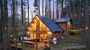 Una cabaña de madera con terraza, jacuzzi y chimenea de piedra.