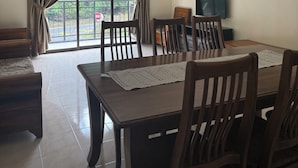 A dining area with a table, chairs, a chandelier, a television, and a painting on the wall.