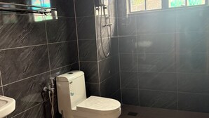 A bathroom with a toilet, a sink, a shower, and a window with a view of greenery.