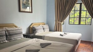 A hotel room with two beds, a framed picture on the wall, a window with curtains, and a wooden floor.