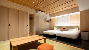 Een hotelkamer met een houten plafond, twee bedden, een klein tafeltje en een futon.
