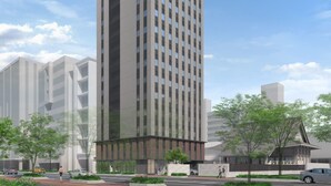 Een modern hoog gebouw met een opvallend logo bovenaan, omgeven door groen en andere gebouwen.