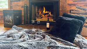 Une pièce chaleureuse avec une cheminée, un plaid en fourrure, une valise et deux verres à vin.