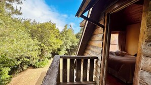 Une cabane en bois dotée d’un balcon, avec un lit à l’intérieur, et offrant une vue sur les arbres environnants.