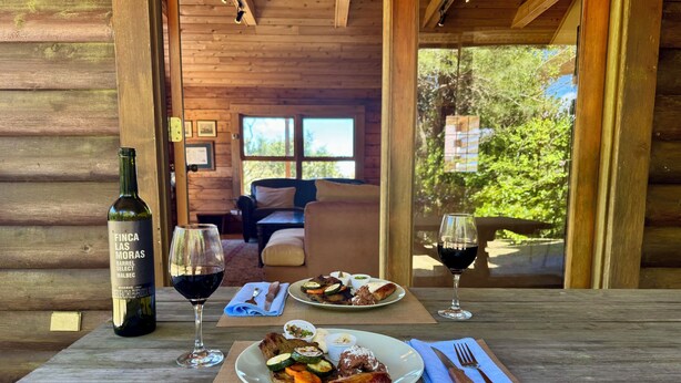 Une table en bois avec une bouteille de vin, deux verres, une assiette de nourriture et des couverts.