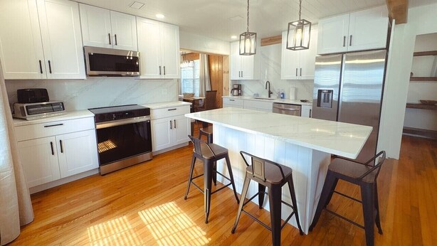 Een moderne keuken met witte kasten, roestvrijstalen apparatuur en een centraal eiland met barstoelen.