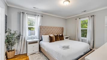 A bedroom with a bed, bedside tables, a nightstand, a window with curtains, a potted plant, and a ceiling light.