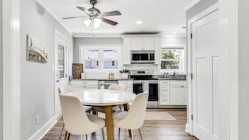 A kitchen with white cabinets, a microwave, a stove, and a ceiling fan. There is a dining table with chairs.