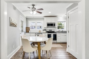 A kitchen with white cabinets, a microwave, a stove, and a ceiling fan. There is a dining table with chairs.