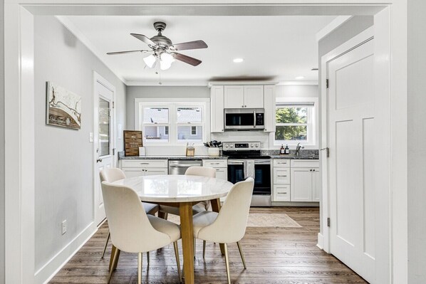 A kitchen with white cabinets, a microwave, a stove, and a ceiling fan. There is a dining table with chairs.
