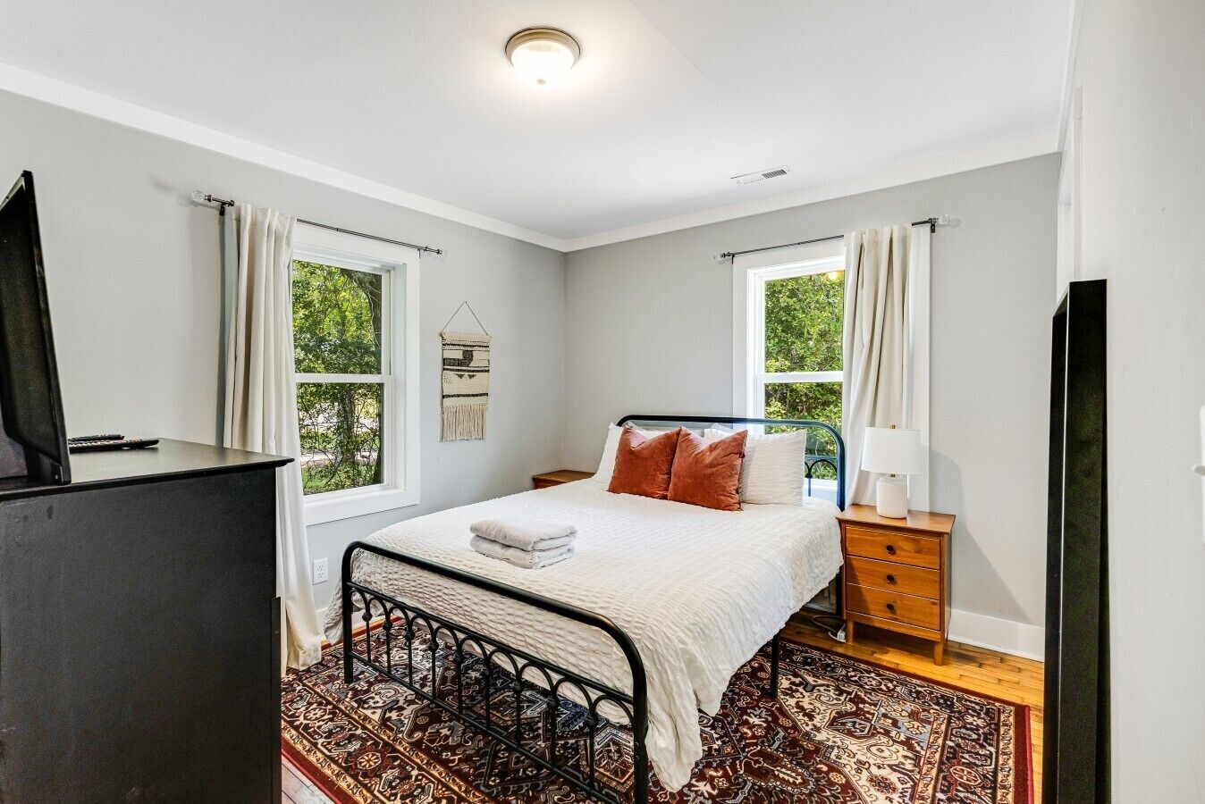 A bedroom with a bed, bedside tables, a TV, and a window.