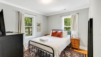 A bedroom with a bed, bedside tables, a TV, and a window.