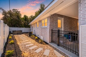 Um imóvel residencial com fachada de tijolos, caminho pavimentado e quintal cercado.