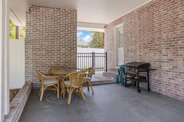 An outdoor patio with a brick wall, a round table with wicker chairs, and a barbecue grill.