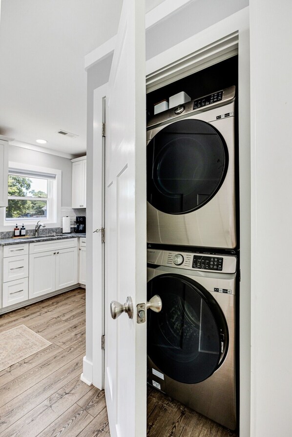 A modern kitchen with white cabinets, a built-in washer and dryer, and a window with a view of greenery.