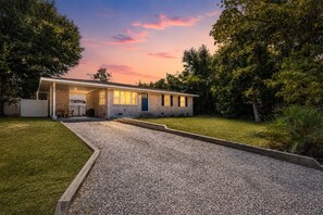 A single-story house with a covered porch, a gravel driveway, and a well-maintained lawn.