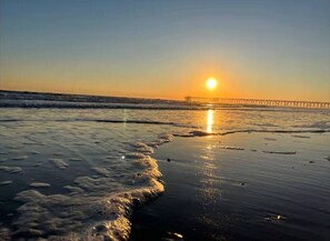 Une plage avec un coucher de soleil, des vagues et une jetée au loin.