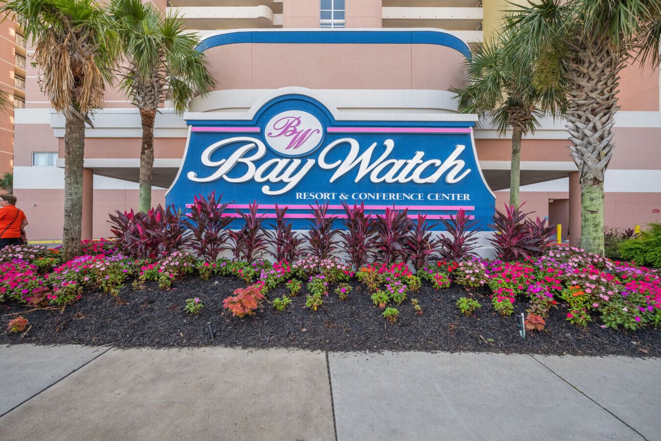 Schild für das Bay Watch Resort & Conference Center mit einem bunten Blumenbeet im Vordergrund.
