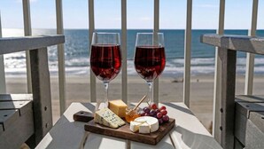 Une vue sur la mer, avec deux verres de vin rouge, du fromage, des raisins et un pot de miel sur une table.
