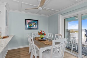 Comedor con mesa de madera, sillas blancas, ventilador de techo y vistas al exterior.