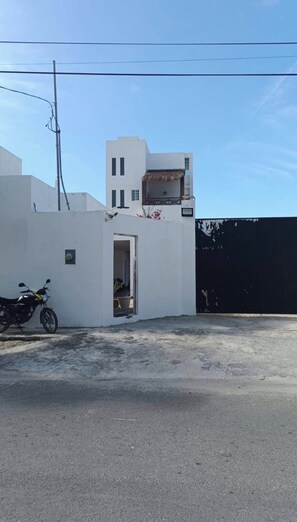 A white building with a small balcony, a motorcycle parked in front, and a clear sky.