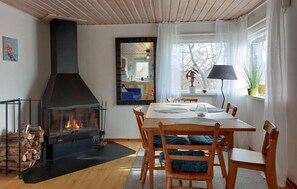 Een gezellige woonkamer met een open haard, een eettafel met stoelen, een groot raam met gordijnen en uitzicht op het omliggende landschap.