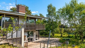 Ein modernes Haus mit Terrasse, Grillplatz und einem großen Fenster mit Blick auf einen Garten.
