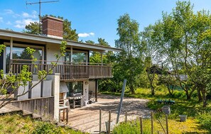 Une maison moderne dotée d’une terrasse, d’un espace barbecue et d’une grande fenêtre donnant sur un jardin.