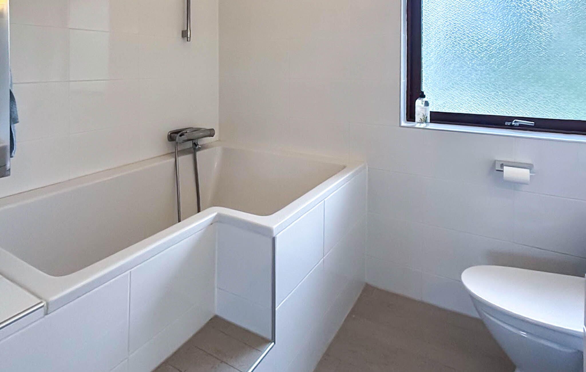 Une salle de bain avec une baignoire blanche, des toilettes et une fenêtre.