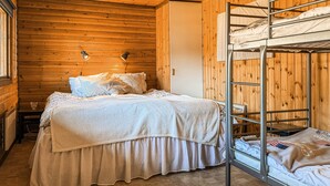 Een slaapkamer met stapelbedden, houten wanden, een bed met een witte dekbedovertrek en twee wandlampen.