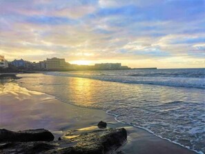 A beach with waves, a sunset, and buildings in the background. - Tenerife Sur El Médano Vacaciones - 3a (Medano, El)