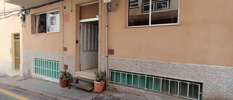 A building with a gated entrance, a window with a metal grill, and a potted plant on the sidewalk.