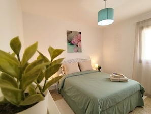 A bedroom with a bed, a bedside table, a lamp, a wall-mounted picture, and a potted plant. - Tenerife Sur El Médano Vacaciones - 3a (Medano, El)