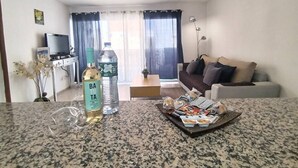 Sala de estar com sofá, mesa de centro, televisão e área de cozinha ao fundo.
