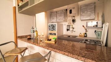 A kitchen with a granite countertop, white cabinets, and a built-in oven. There are two chairs and a shelf with decorative items.
