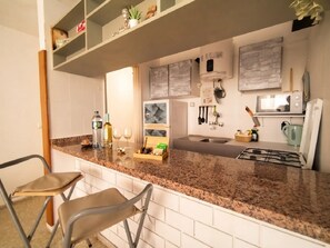 Eine Küche mit Granit Arbeitsplatte, weißen Schränken und einem eingebauten Backofen. Zwei Stühle und ein Regal mit Dekorationselementen sind vorhanden.