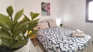 Quarto com cama, planta em vaso, quadro na parede e luminária pendente.