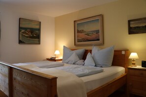 A wooden bed with white linens, two bedside tables with lamps, and two framed landscape paintings on the wall. - Apartment (B) with 1 bedroom and terrace 1-2 persons (Chieming)