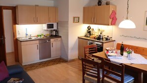 A compact kitchen with wooden cabinets, a microwave, and a dining area with a table set for two. - Vacation apartment (D) 1 bedroom and balcony, 1-4 persons (Chieming)
