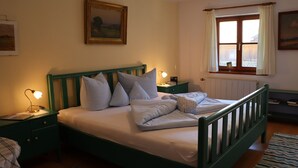 A neatly made bed with pillows and a bedside lamp, a framed picture on the wall, and a window with curtains. - Vacation apartment (D) 1 bedroom and balcony, 1-4 persons (Chieming)