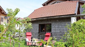 Una casa rústica amb teulada vermella, façana de fusta i un jardí ple de flors vermelles i verdura.