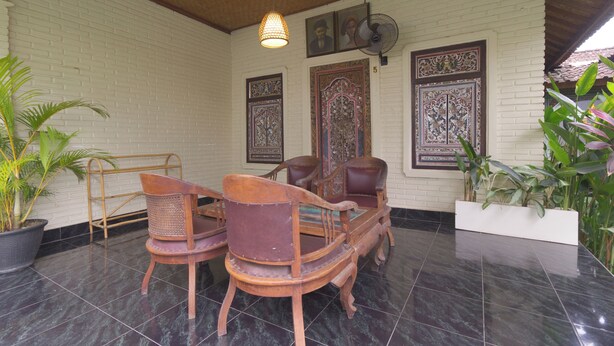 A room with a tiled floor, two wooden chairs, a potted plant, and a wall with decorative panels. - Villa Markisa (Ubud)