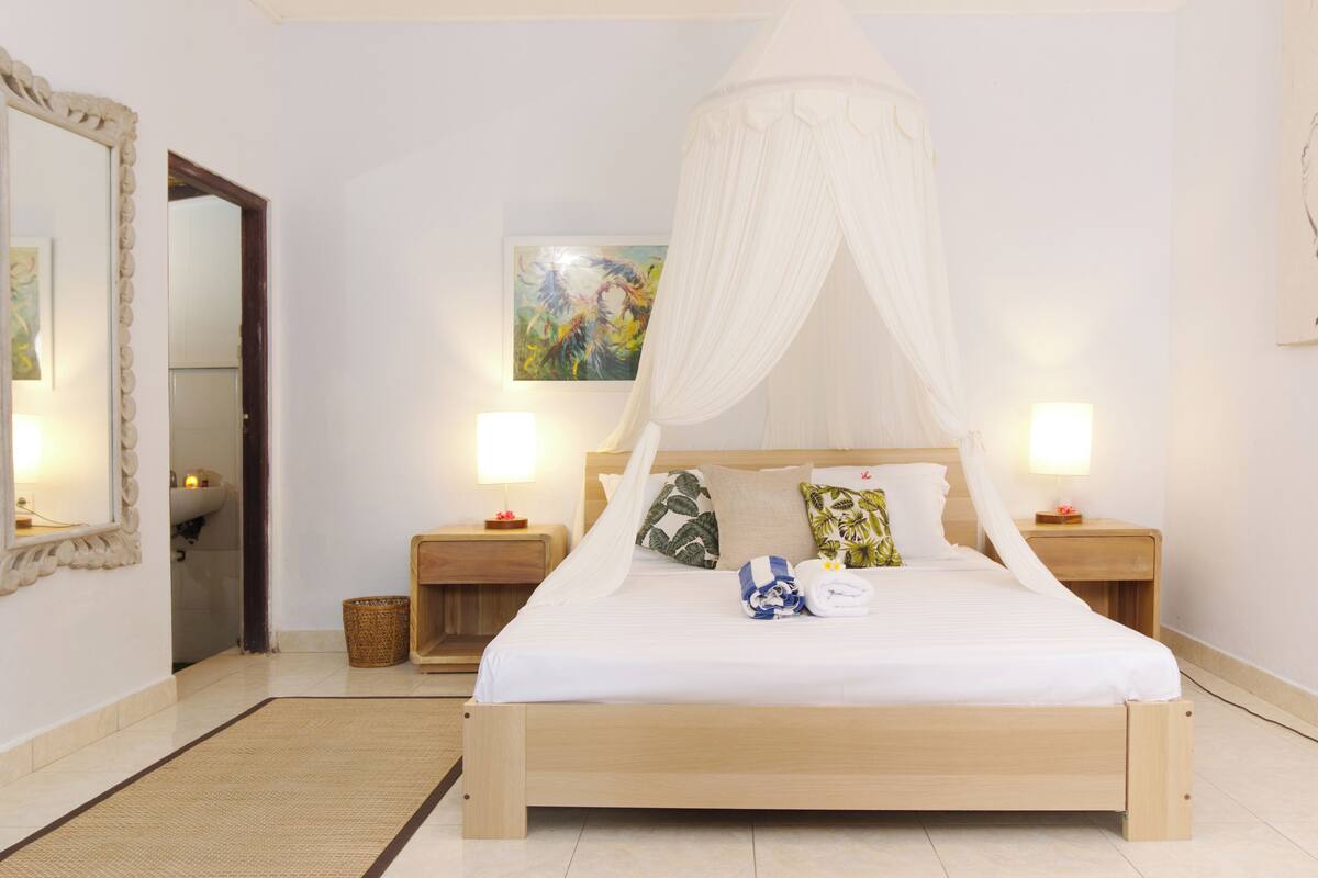 Une chambre à coucher avec un lit à baldaquin, des lampes de chevet, un tableau au mur et un miroir doté d’un cadre décoratif.