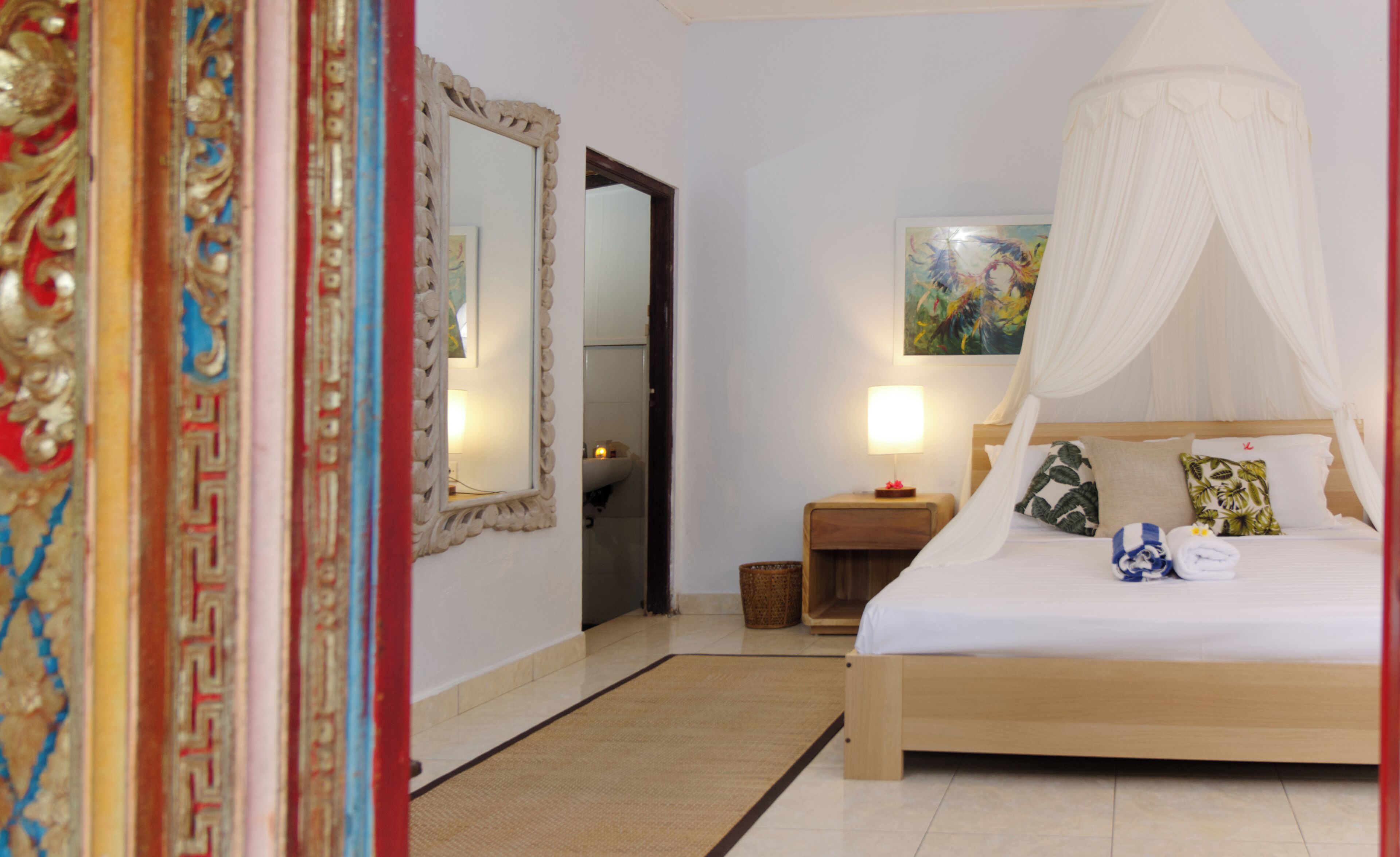 A bedroom with a bed, a nightstand, a lamp, a mirror, and a painting on the wall.