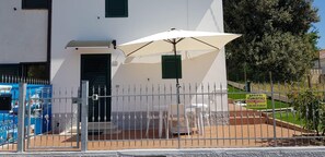A white building with a gated entrance, a white umbrella, and outdoor seating. - Bilo Maria Grazia - delightful app.to with air condiizonata (Numana)