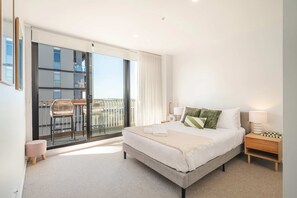 Una habitación de hotel moderna con una cama grande, un balcón con mesa y sillas, y vista a la ciudad.