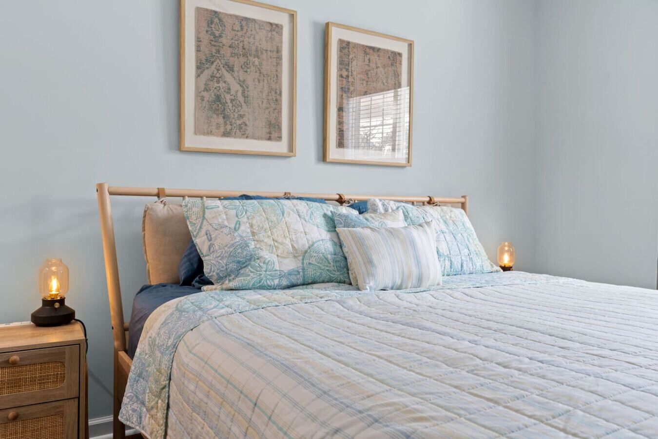 A bedroom with a bed, two wall-mounted pictures, a bedside lamp, and a nightstand.