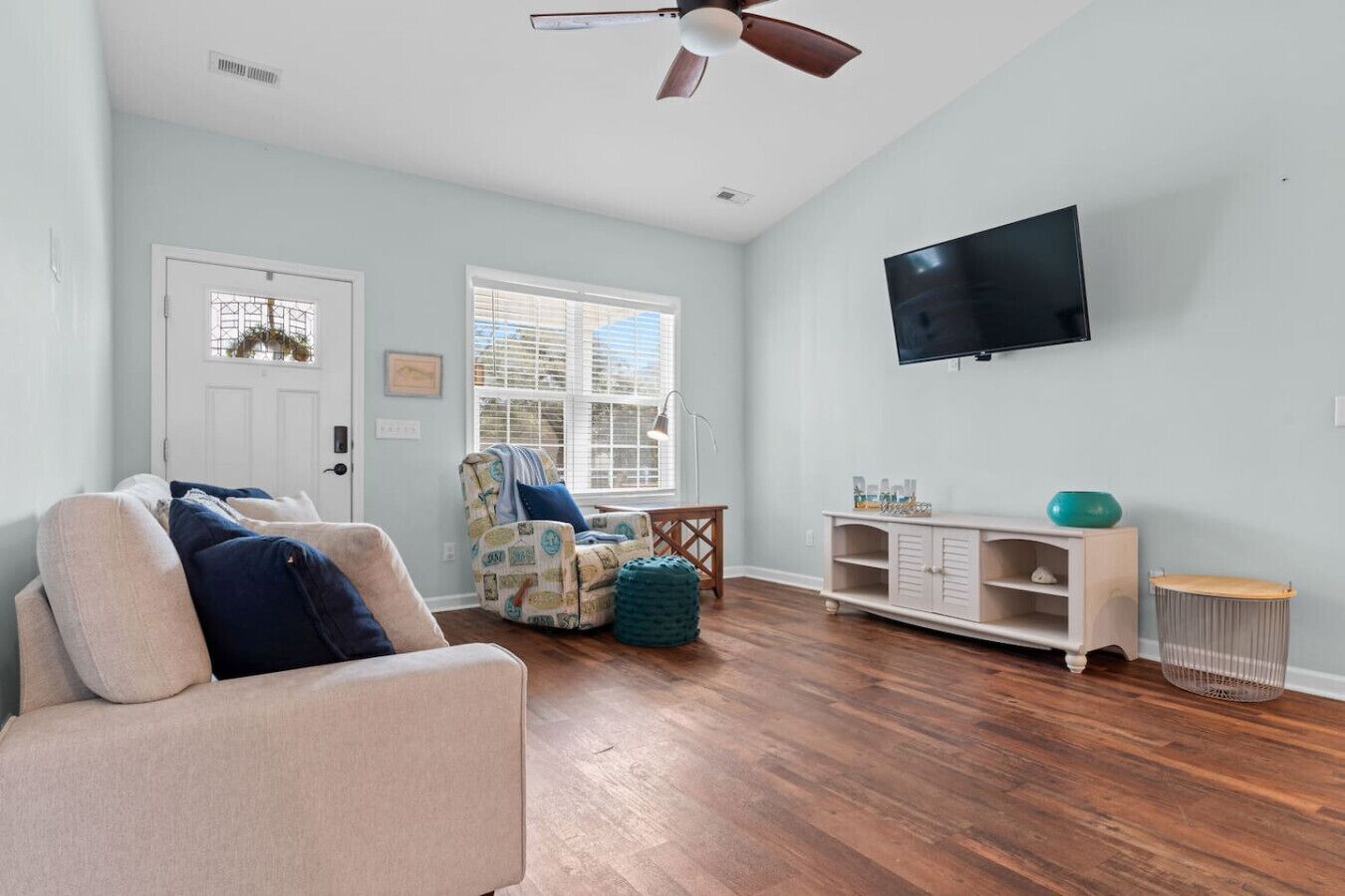 A living room with a sofa, a chair, a TV, and a wooden floor.